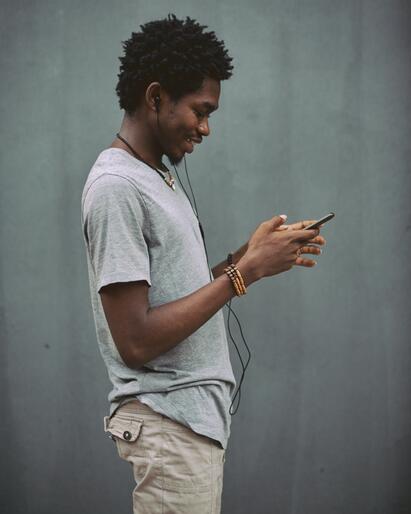 En mann står ved en grå vegg og ser på mobiltelefonen sin